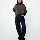 Person wearing a brown turtleneck sweater and dark jeans on a white background