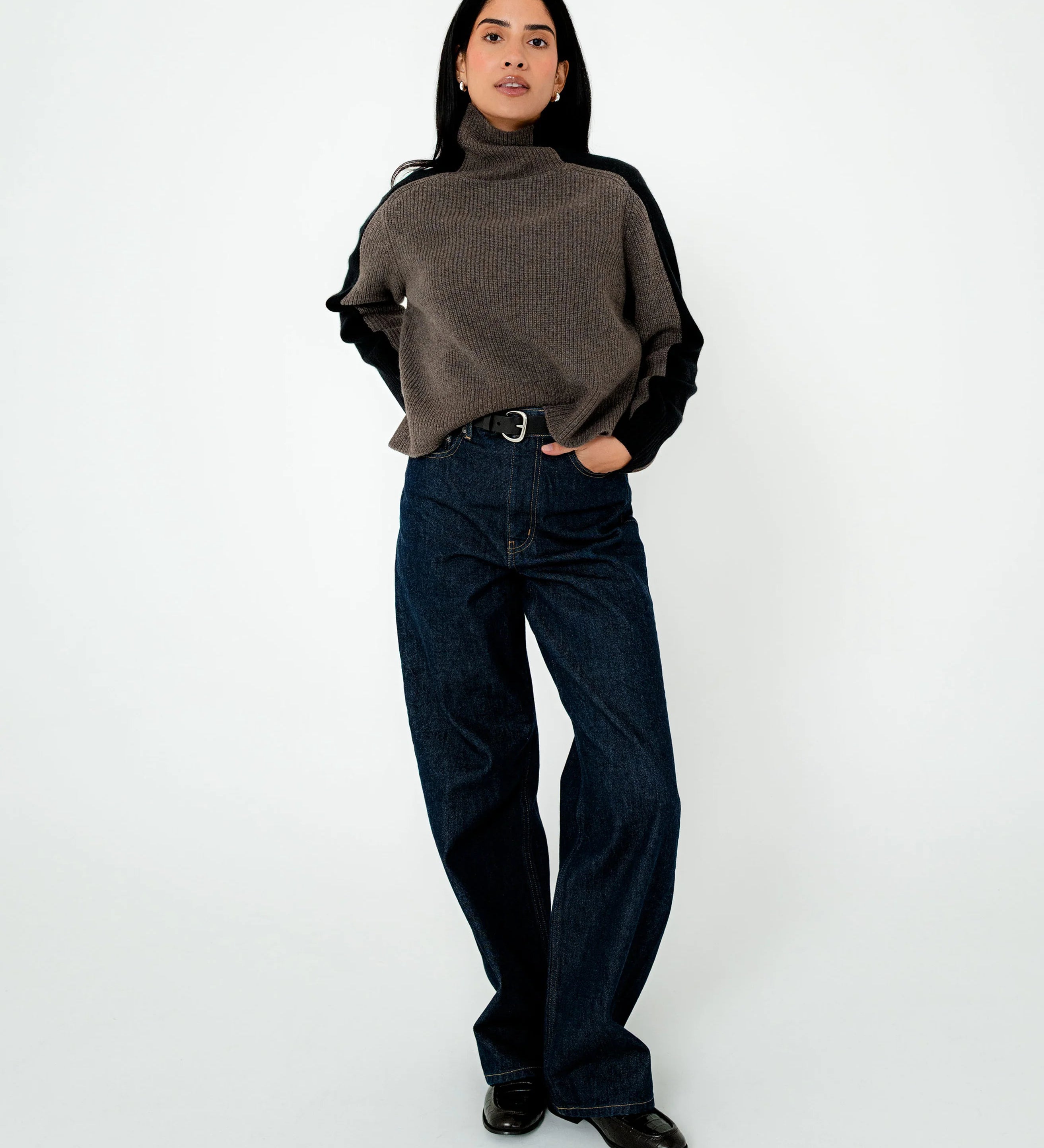 Person wearing a brown turtleneck sweater and dark jeans on a white background
