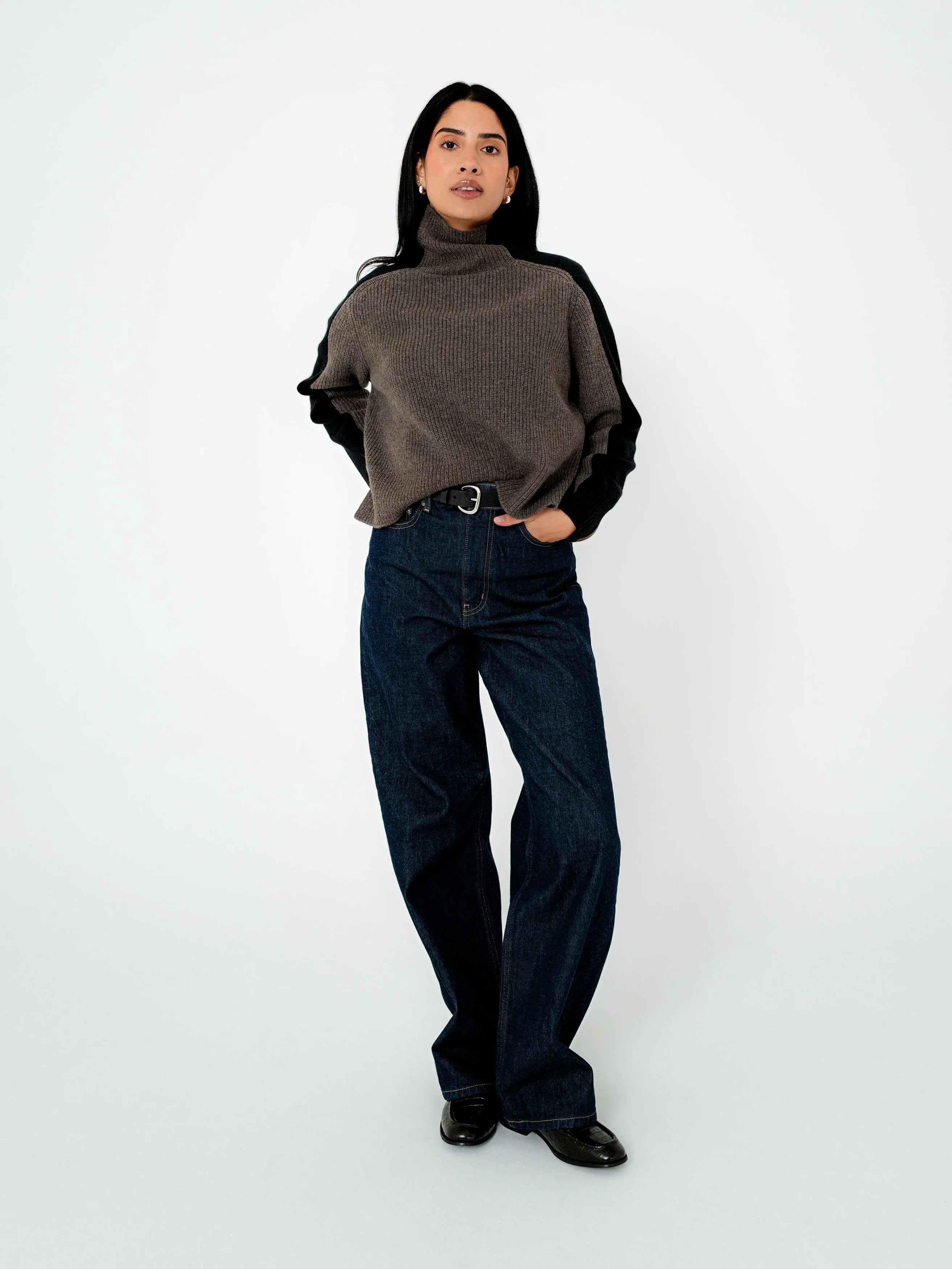 Person wearing a brown turtleneck sweater and dark jeans on a white background