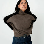 Woman wearing a brown turtleneck sweater with black sleeves on a white background