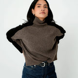 Woman wearing a brown turtleneck sweater with black sleeves on a white background