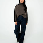 Person wearing a brown turtleneck sweater and dark jeans on a white background