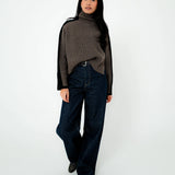 Person wearing a brown turtleneck sweater and dark jeans on a white background