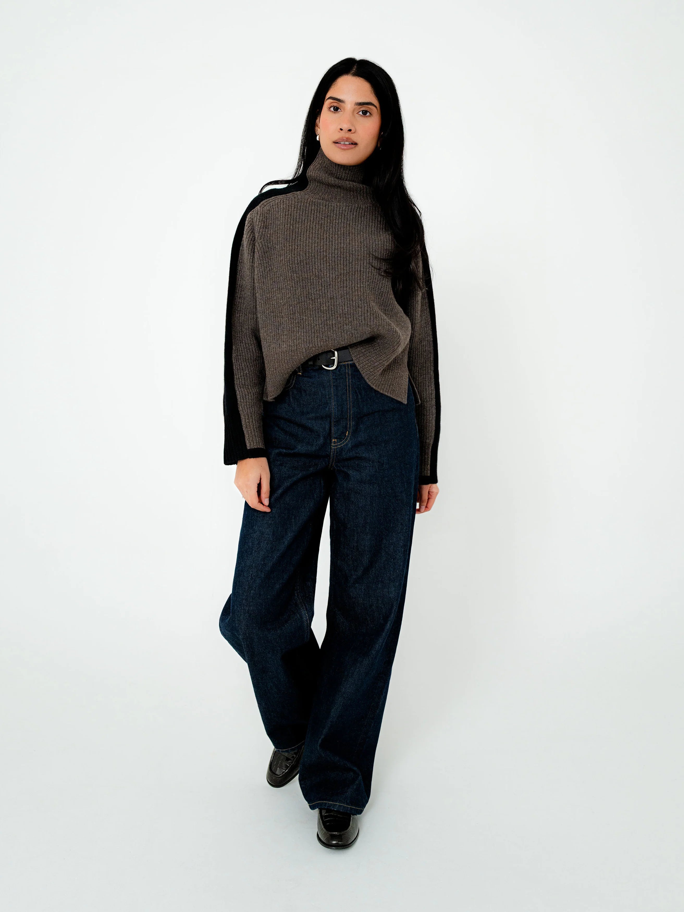 Person wearing a brown turtleneck sweater and dark jeans on a white background