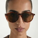 Person wearing tortoiseshell sunglasses with a neutral background