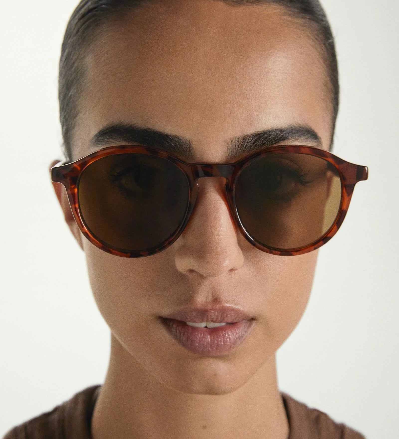 Person wearing tortoiseshell sunglasses with a neutral background
