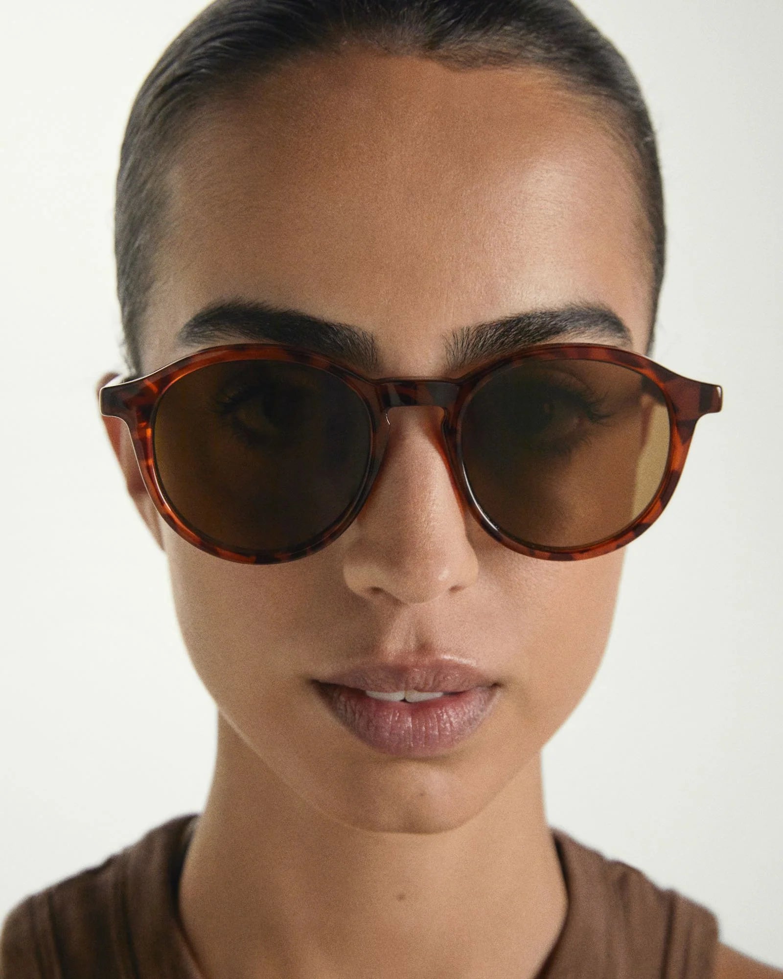 Person wearing tortoiseshell sunglasses with a neutral background