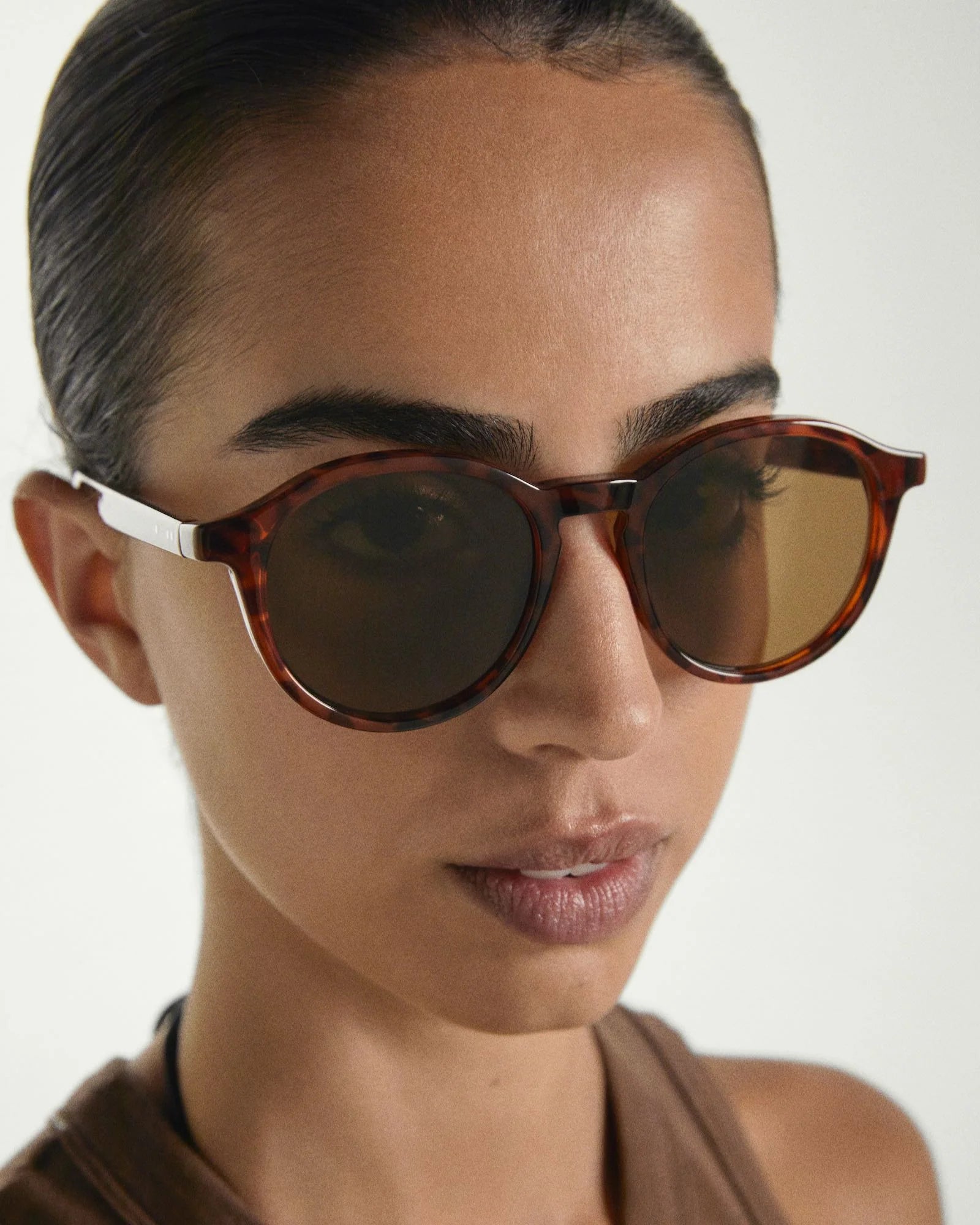 Close-up of a person wearing brown sunglasses with a neutral background