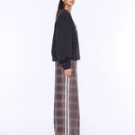A model wearing a black crewneck sweatshirt and a brown wide-leg pleated skirt with a white side stripe, photographed against a plain white studio background.
