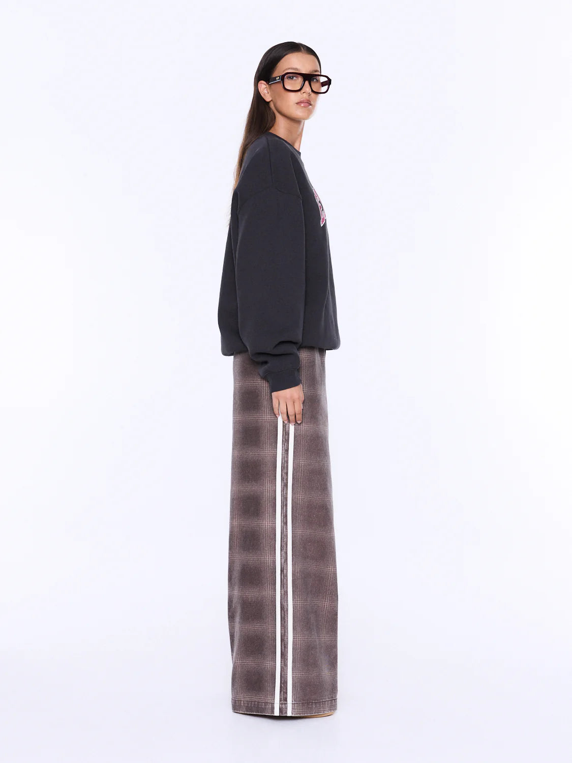 A model wearing a black crewneck sweatshirt and a brown wide-leg pleated skirt with a white side stripe, photographed against a plain white studio background.