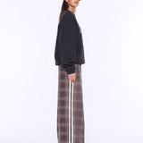 A model wearing a black crewneck sweatshirt and a brown wide-leg pleated skirt with a white side stripe, photographed against a plain white studio background.