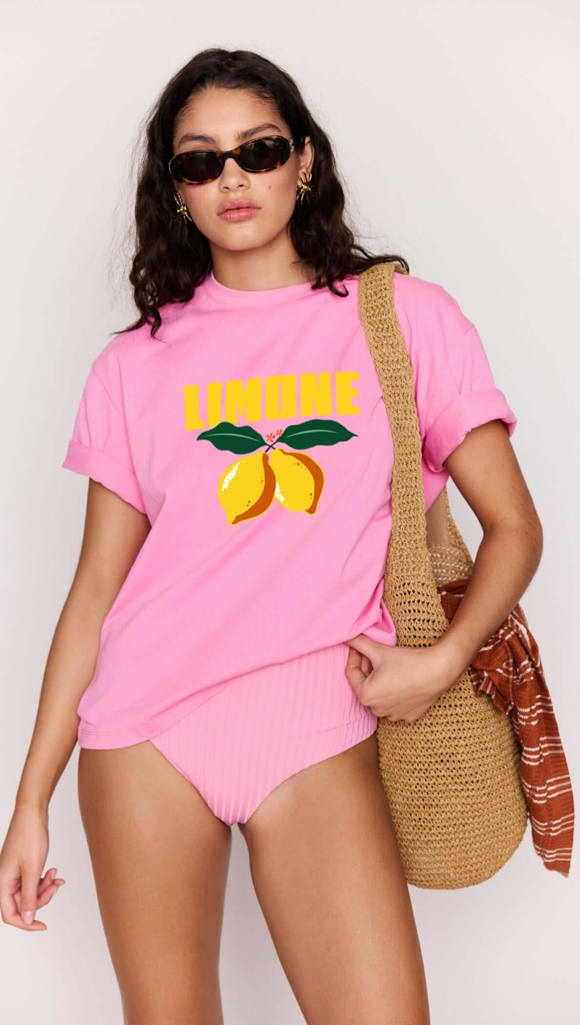 Woman wearing a pink t-shirt with 'Limone' design and sunglasses, holding a straw bag.