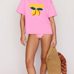 Person wearing a pink t-shirt with lemon design and matching shorts, holding a woven bag.
