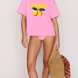 Person wearing a pink t-shirt with lemon design and matching shorts, holding a woven bag.