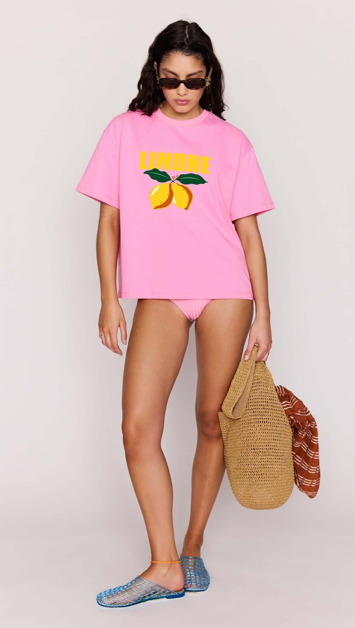 Person wearing a pink t-shirt with lemon design and matching shorts, holding a woven bag.