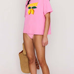 Woman wearing a pink t-shirt with a yellow graphic design on a plain background