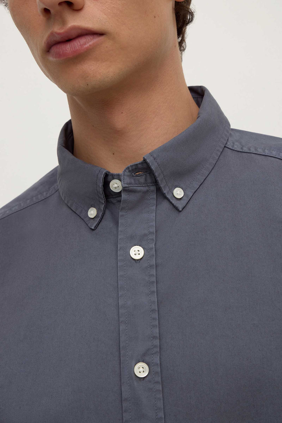 Close-up of a person wearing a dark blue button-up shirt with a plain background