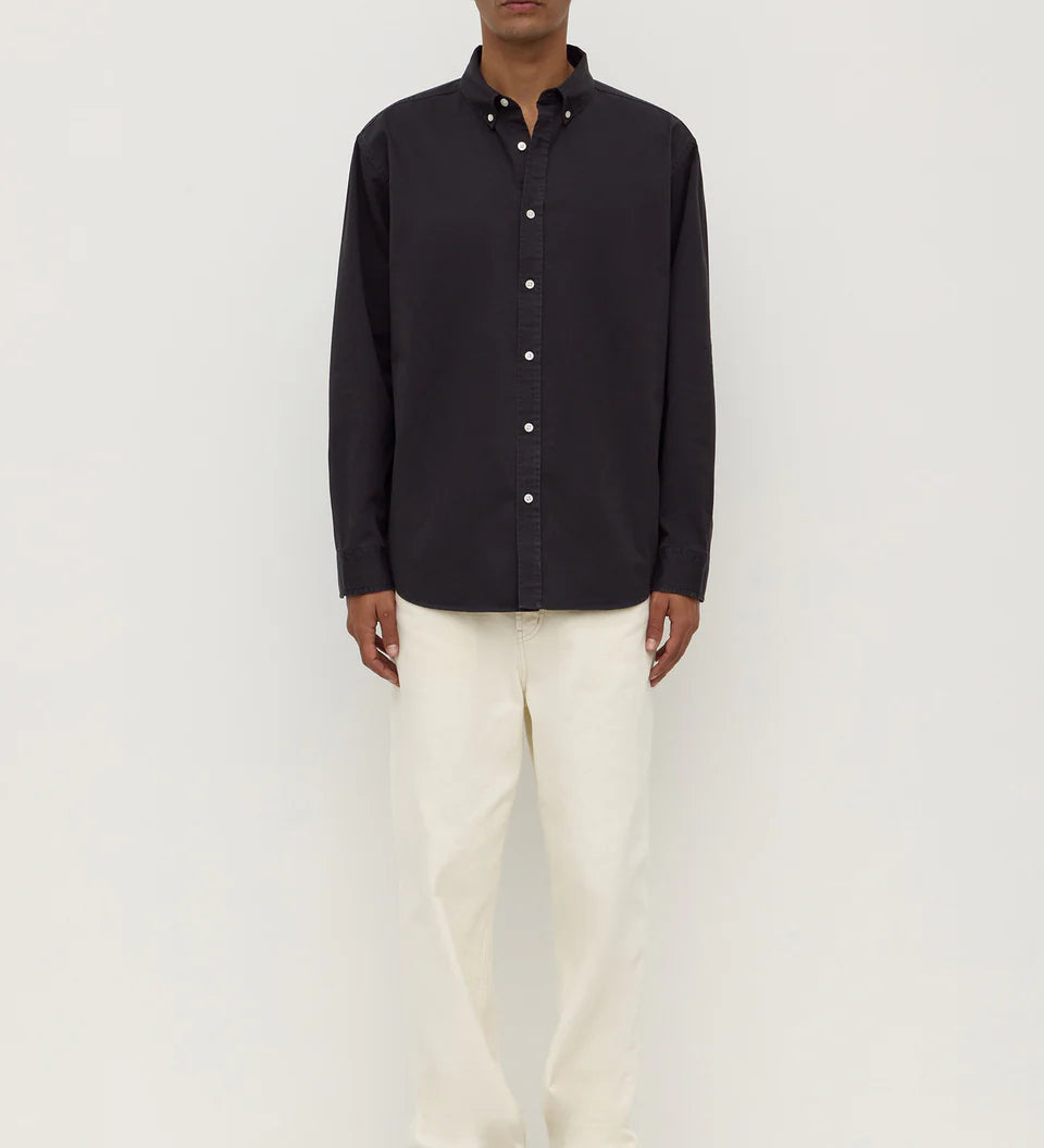 Man wearing a black button-up shirt and white pants on a white background