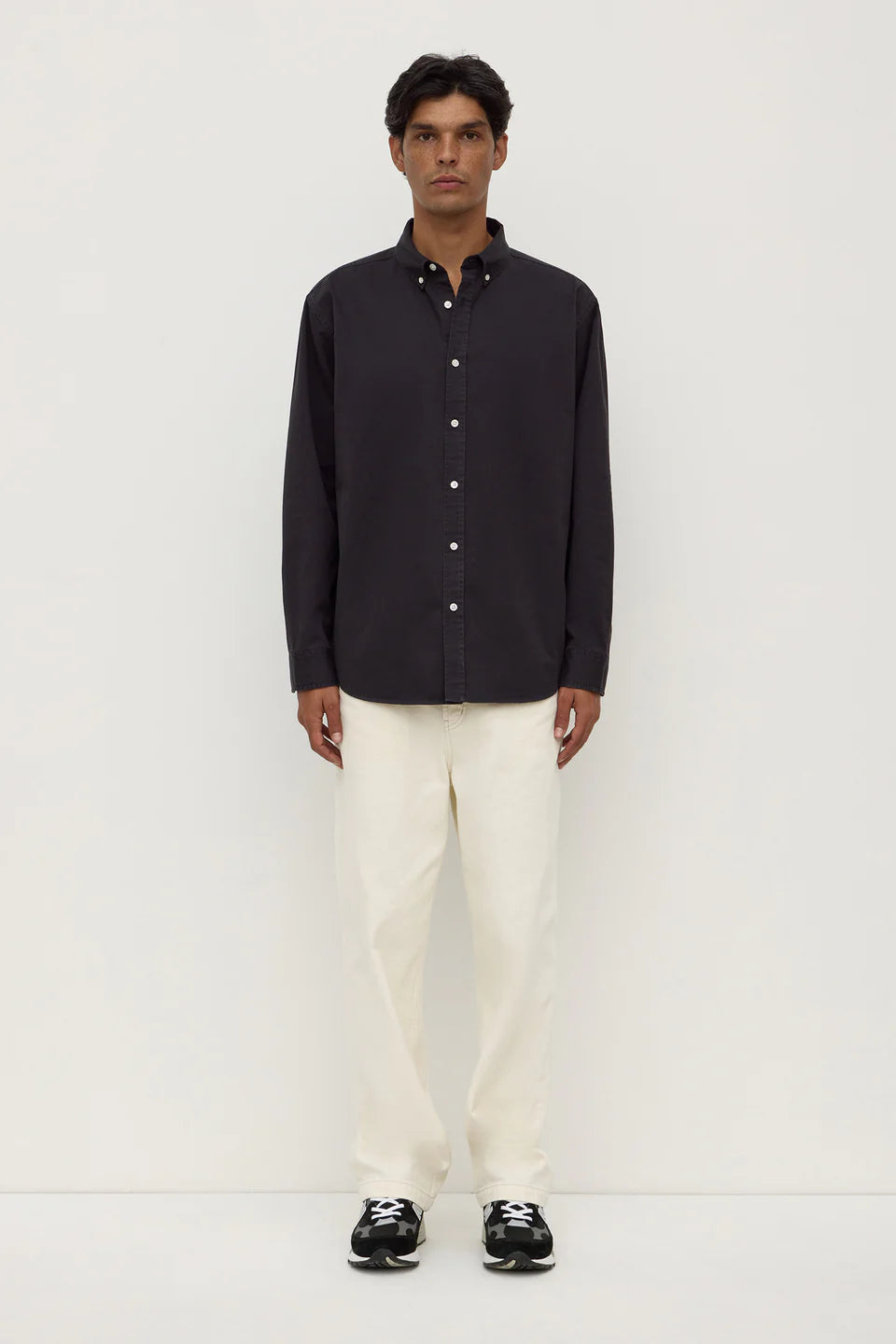 Man wearing a black button-up shirt and white pants on a white background