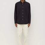 Man wearing a black button-up shirt and white pants on a white background