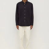 Man wearing a black button-up shirt and white pants on a white background