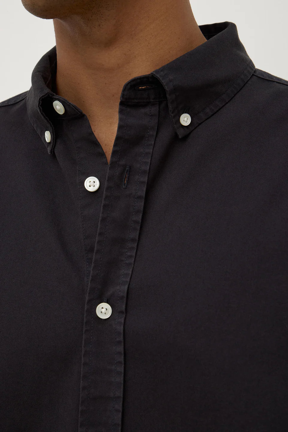 Close-up of a black button-up shirt with white buttons on a neutral background