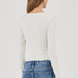 Woman wearing a white textured Top and blue jeans on a plain background