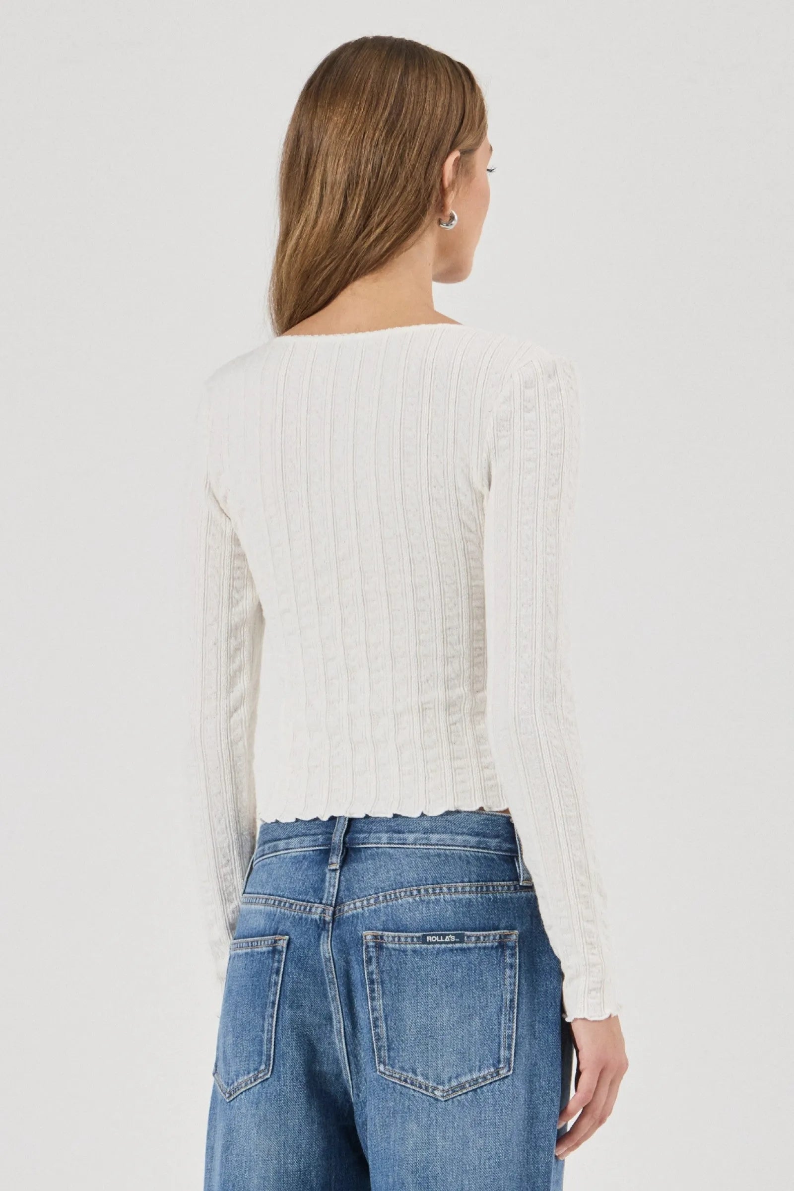 Woman wearing a white textured Top and blue jeans on a plain background