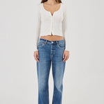Woman wearing a white textured Top and blue jeans on a plain background