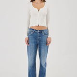 Woman wearing a white textured Top and blue jeans on a plain background