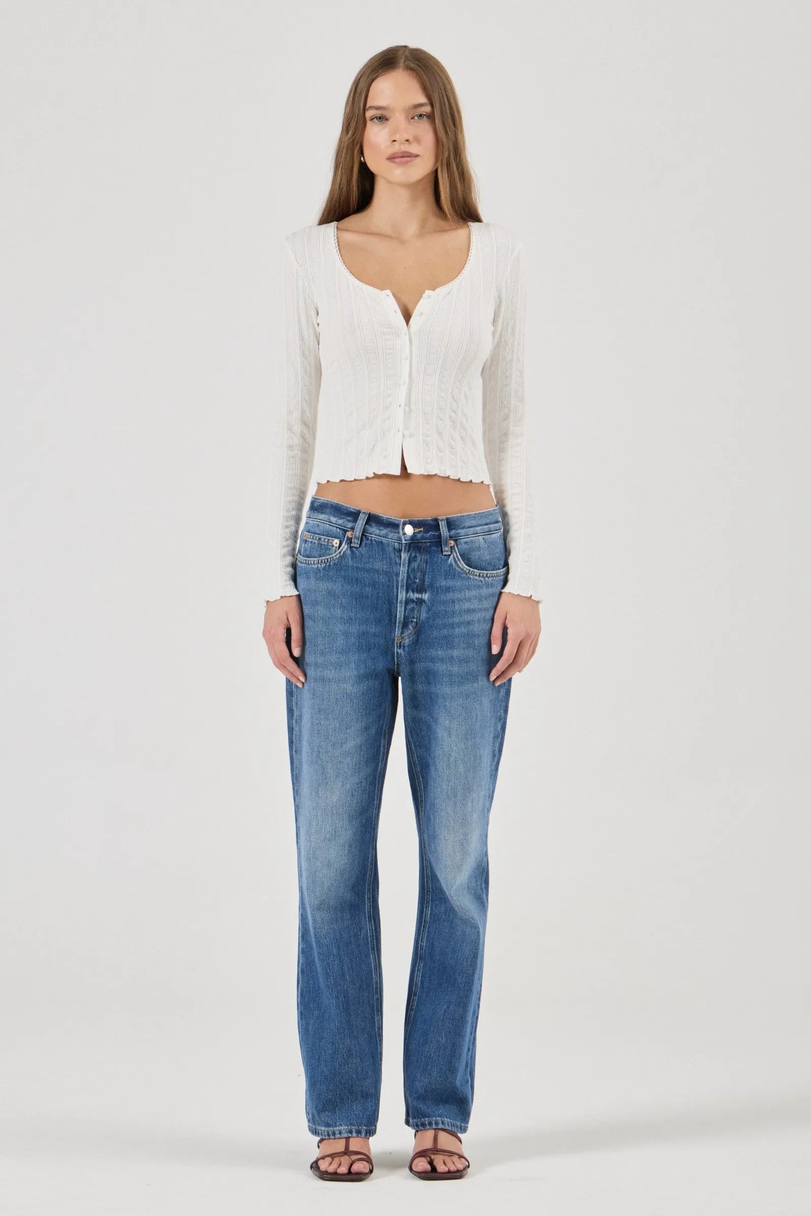 Woman wearing a white textured Top and blue jeans on a plain background