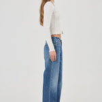 Woman wearing a white textured Top and blue jeans on a plain background