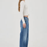 Woman wearing a white textured Top and blue jeans on a plain background