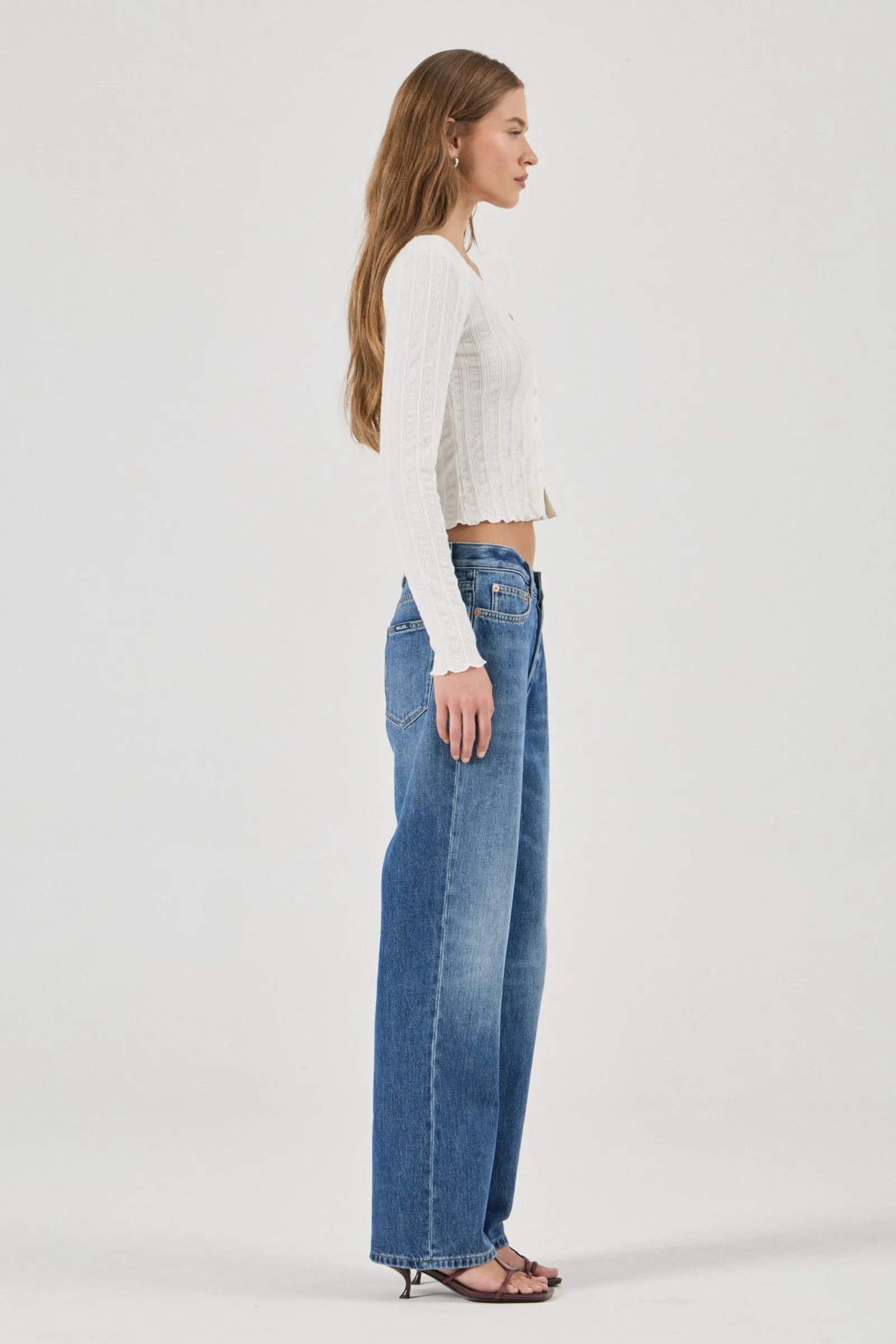 Woman wearing a white textured Top and blue jeans on a plain background