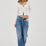 Woman wearing a white textured Top and blue jeans on a plain background