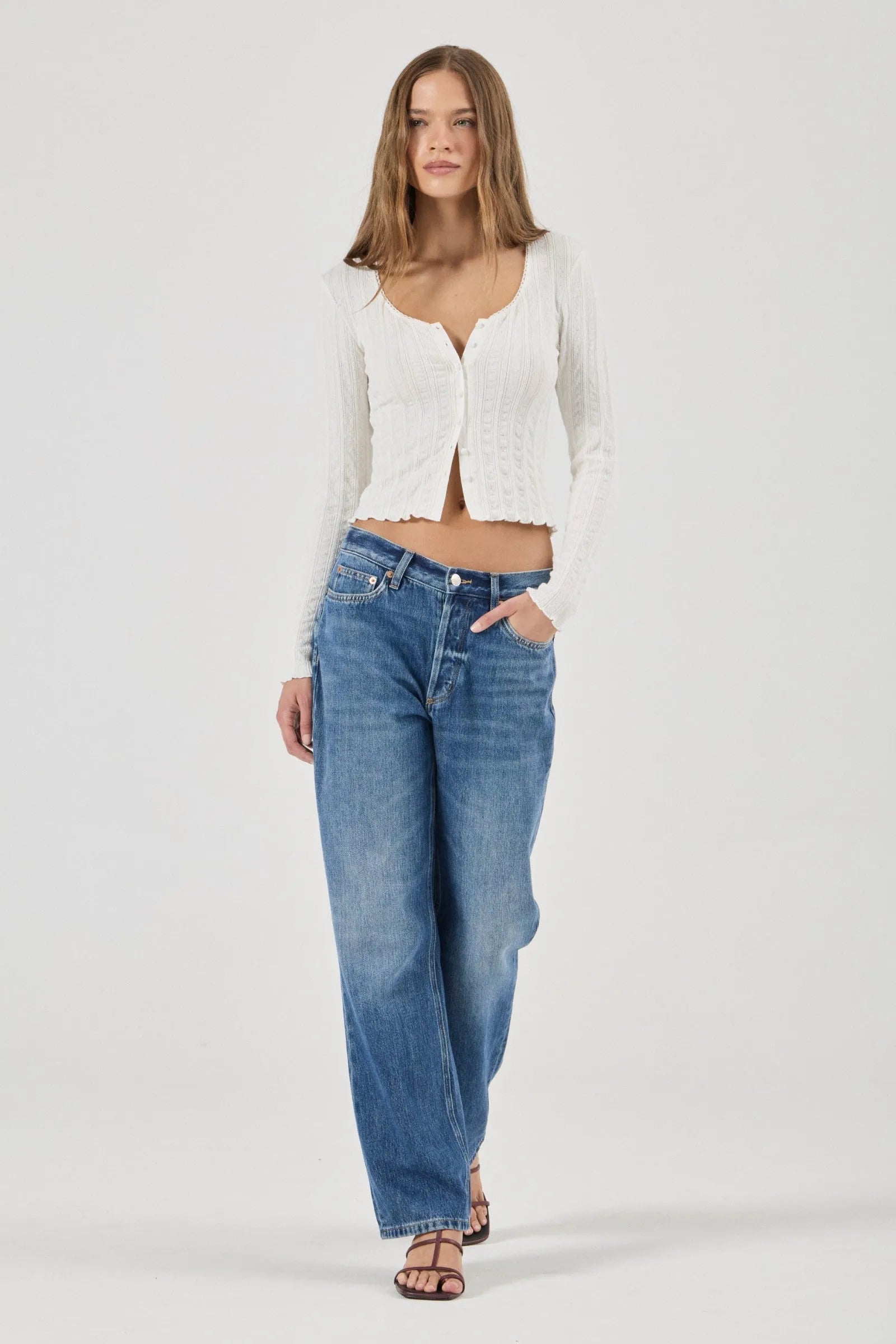 Woman wearing a white textured Top and blue jeans on a plain background