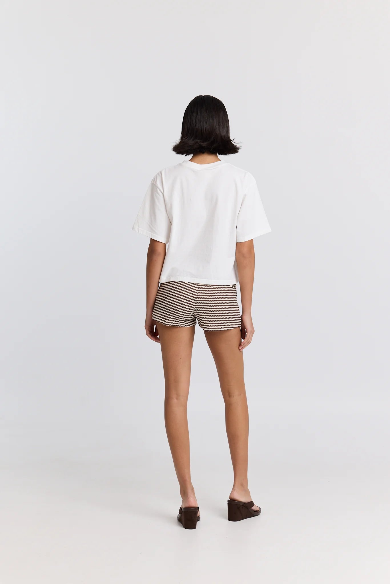 Person wearing a white top and striped shorts on a plain background