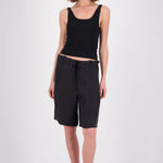 A model wearing a black ribbed tank top and black drawstring shorts, styled with black sunglasses and black sandals, standing against a light gray studio background.