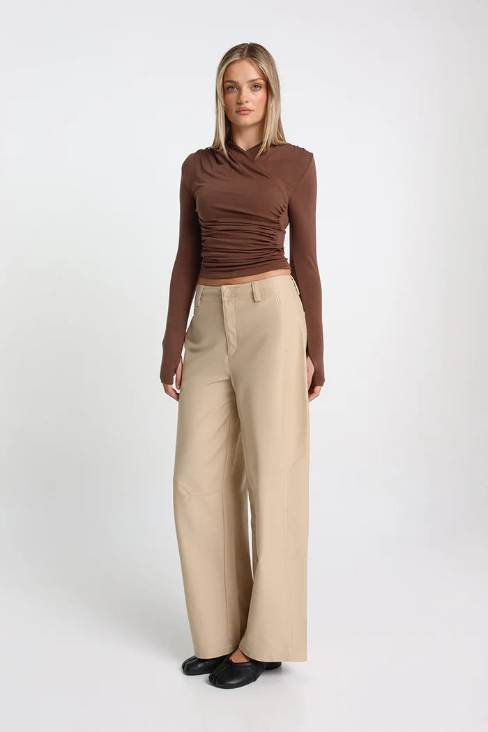 Woman wearing a brown long-sleeve top and beige wide-leg pants on a white background