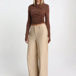 Woman wearing a brown long-sleeve top and beige wide-leg pants on a white background