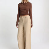 Woman wearing a brown long-sleeve top and beige wide-leg pants on a white background