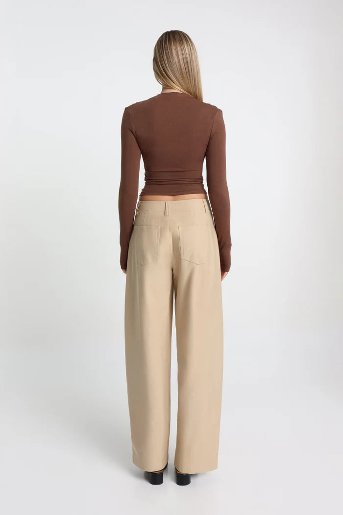 Woman wearing a brown long-sleeve top and beige wide-leg pants on a white background