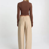 Woman wearing a brown long-sleeve top and beige wide-leg pants on a white background