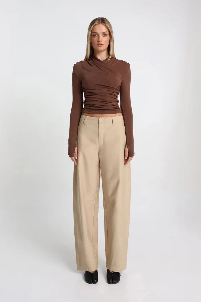 Woman wearing a brown long-sleeve top and beige pants on a white background
