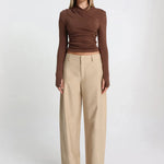 Woman wearing a brown long-sleeve top and beige pants on a white background