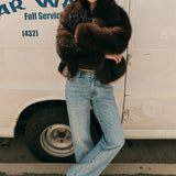 Person wearing a fur coat and jeans standing in front of a van with 'Warren' branding.
