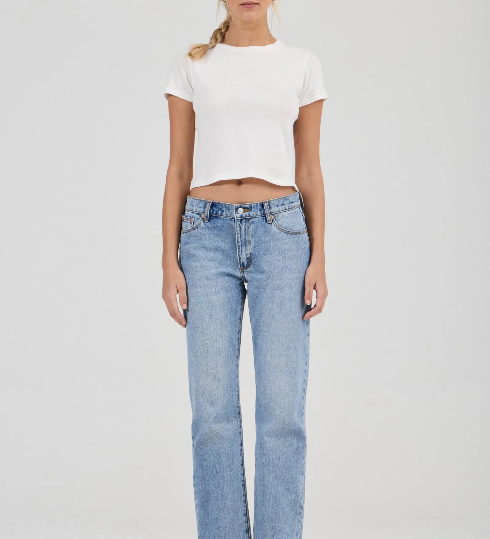 Woman wearing a white t-shirt and light blue jeans on a plain background