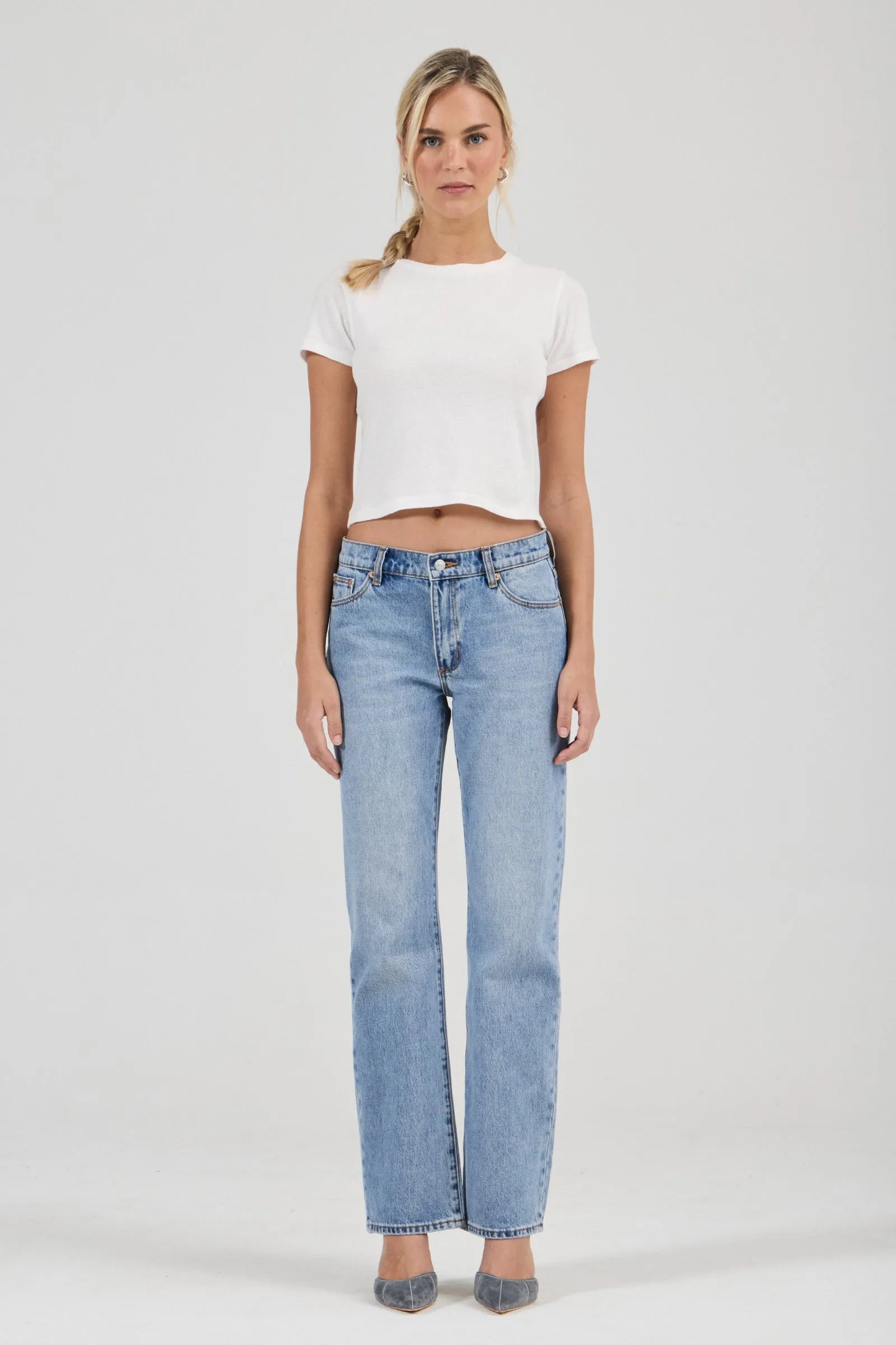 Woman wearing a white t-shirt and light blue jeans on a plain background