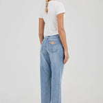 Woman wearing light blue jeans and a white t-shirt on a plain background