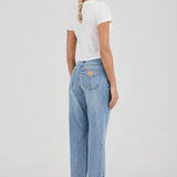 Woman wearing light blue jeans and a white t-shirt on a plain background